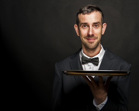 Waiter in black suit holding tray over black background.の写真素材