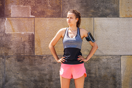 fitness, sport and lifestyle concept - young woman with earphones standing and listening music...