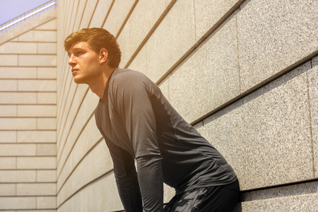 Male jogger resting after morning run while standing against wall background with copy space area...