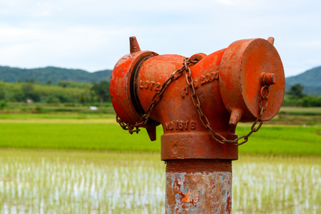 A weathered red fire hydrant emergency water supply near a paddy field.の写真素材