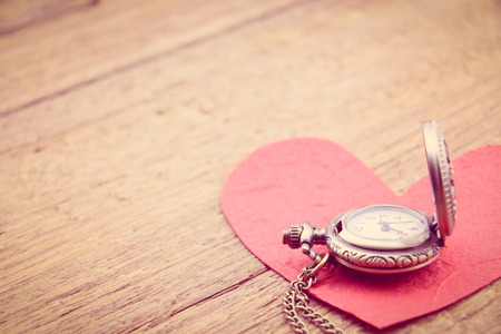 Long necklace antique style pocket watch with a red mulberry paper heart on a wooden surface. A...