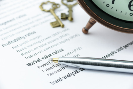 Blue ballpoint pen on a financial ratios analysis check lists with an antique clock and two vintage...