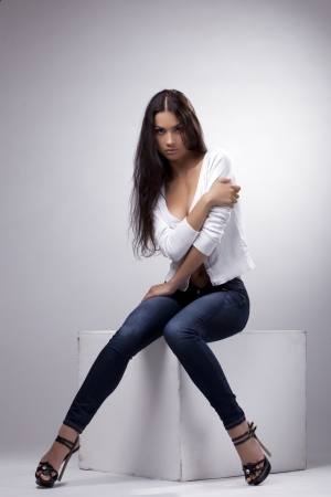 Cute sexy woman sit in jeans and white jacket studio portraitの写真素材