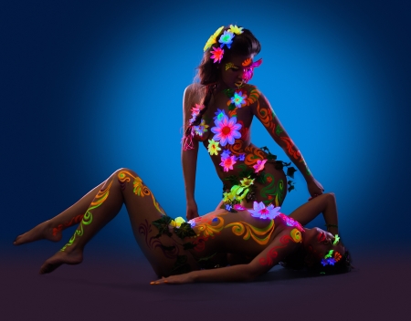 couple of nude women posing with glow ultraviolet body art and flowersの写真素材