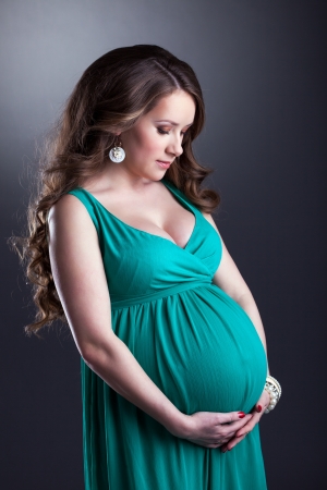 Pretty pregnant woman caressing her belly, on gray backgroundの写真素材