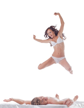 Cheerful slim woman jumping into bed with sexy guy, isolated on whiteの写真素材
