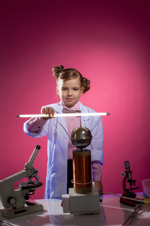 Serious little physicist shows focus with lamp, on pink backgroundの写真素材