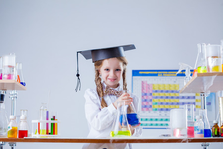 Smiling little girl posing in graduate hat at laboratoryの写真素材