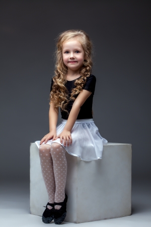 Image of smiling cute girl posing sitting on cube in studioの写真素材