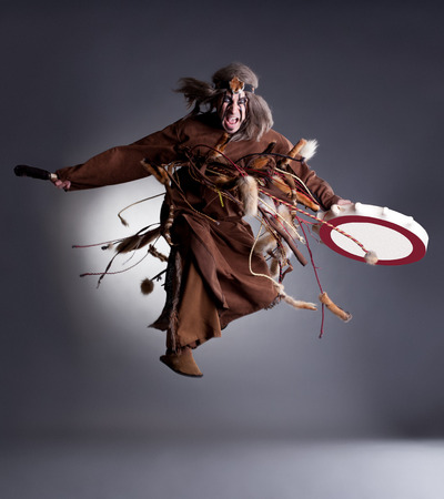 Studio shot of angry shaman posing in jump, on gray background