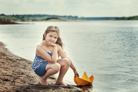 Lovely girl posing with homemade paper boat by lakeの写真素材