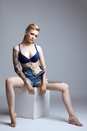 Curvy tattooed model posing sitting on cube in studioの写真素材