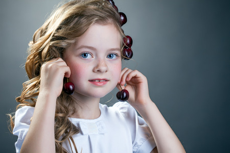 Image of lovely girl tries on cherries as earringsの写真素材