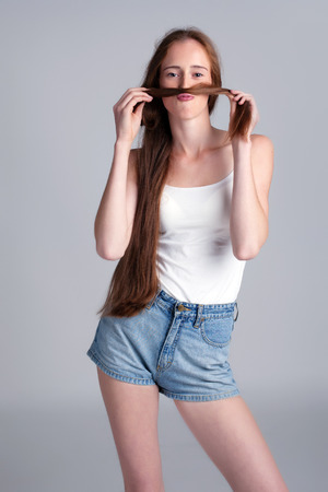 Funny young model fooling around making mustache of her hairの写真素材
