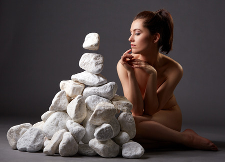 Studio shot of naked woman thoughtfully moves stones by lookの写真素材