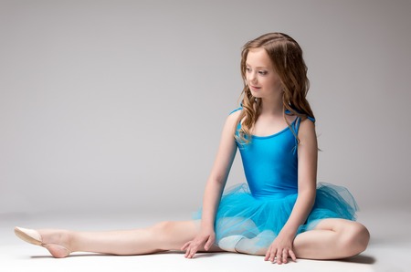 Beautiful little ballerina posing doing stretching, on gray backgroundの写真素材