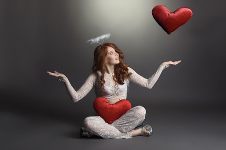 Studio photo of feminine angel playing with hearts, on grey backdropの写真素材