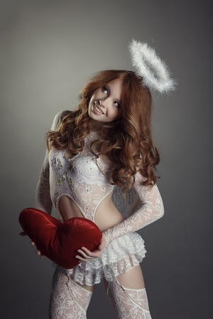 Smiling red-haired beauty posing in angel costume, on grey backgroundの写真素材