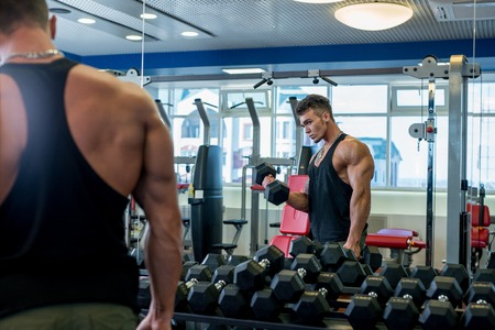 Bodybuilder looks at himself in mirror while exercises with dumbbells