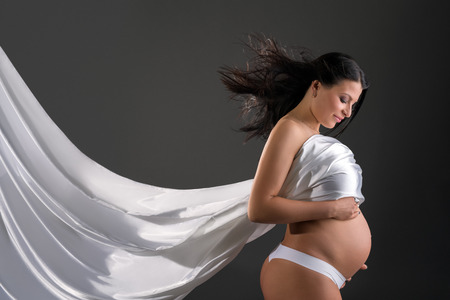 Beautiful pregnant woman poses with fluttering clothの写真素材