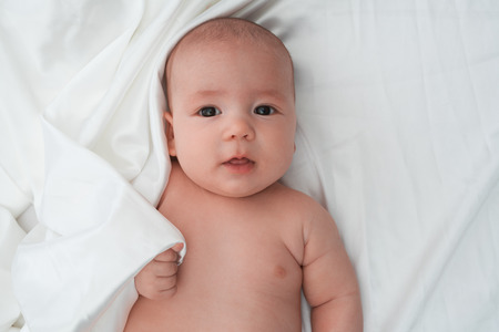 Brown eyed baby boy lying on white linen looking attentively with his tongue stuck out a little close up studio shotの写真素材