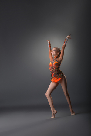 Full length of young athletic gymnast girl in bright leotard exercising on grey studio backgroundの写真素材
