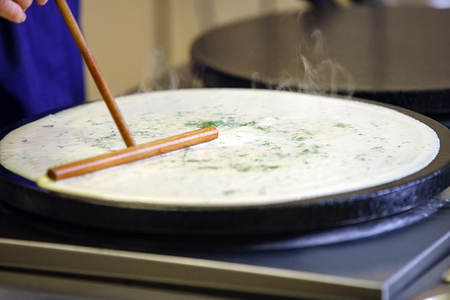 Pancake frying with help of special kitchenware in oil on special pan in cafe kitchenの写真素材