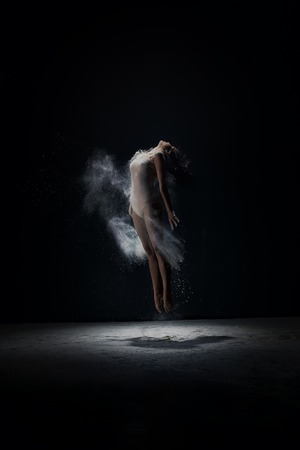 Young girl jumping in white dust cloud in studioの写真素材