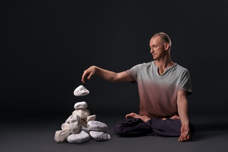 Man sitting in yoga pose with white stones near byの写真素材