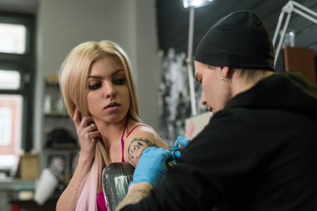 Sexy blonde and tattoo master at work in studioの写真素材