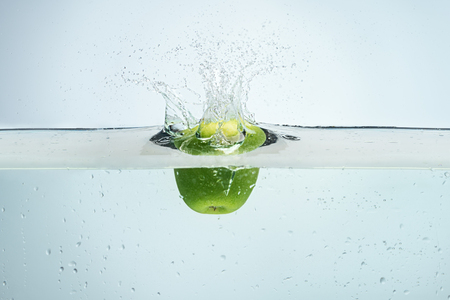 Single apple being dropped into blue waterの写真素材