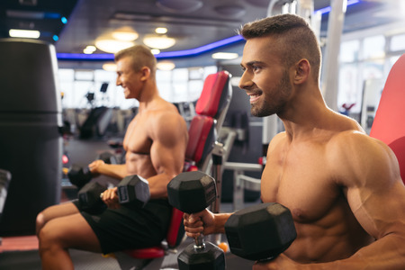 Young muscular men exercising with dumbells in gymの写真素材