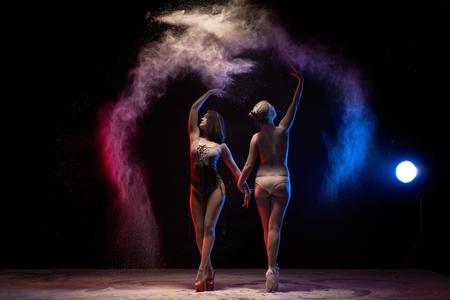 Two girls dancing in color dust cloud in the darkの写真素材
