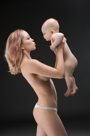 Pretty mother topless holding her baby profile shotの写真素材