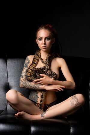 Tattooed woman on the sofa with python shotの写真素材