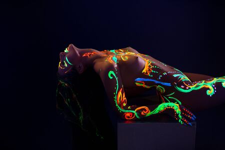 Woman with UV color pattern bodyart in the darkの写真素材