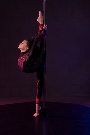 Graceful girl doing gymnastic exercise near pole in darknessの写真素材