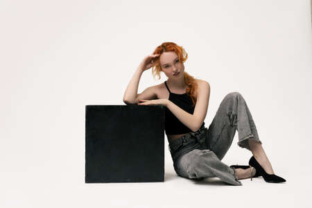Confident young lady sitting on ground and looking at camera