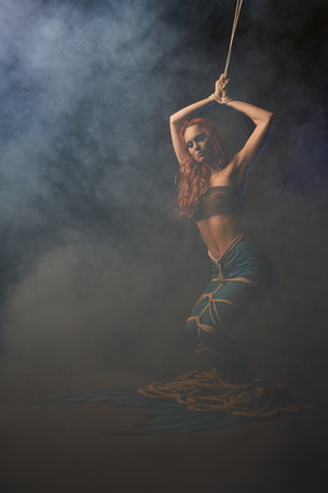 Exhausted mermaid trapped in ropes with smoke in studioの写真素材