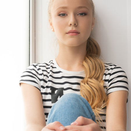 Pretty teenaged blonde sitting on a window sill portraitの写真素材