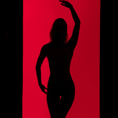 Slim girl dark silhouette dancing against red wallの写真素材