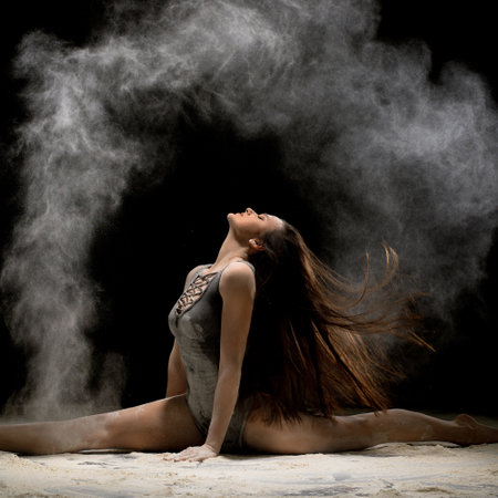 Brunette sitting in a split in dust in the darkの写真素材