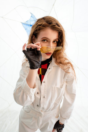 Young Woman Wearing White Jumpsuit and Sunglasses Posing in Studioの写真素材