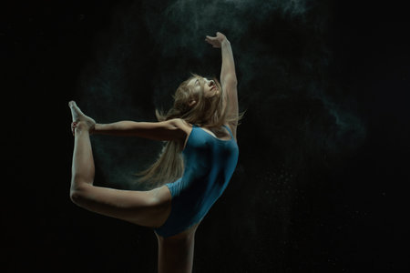 Dancer executing an expressive pose in a dark studio with dust particlesの写真素材