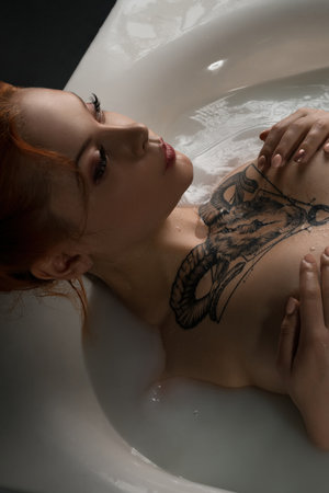 Portrait of a woman relaxing in a bath with intricate tattoo designs