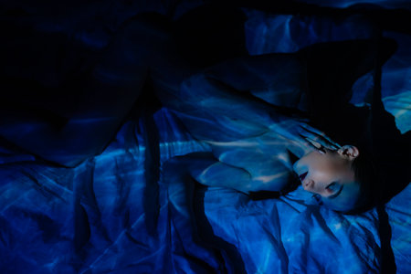 Woman with projected light creating shadows on skin in artistic displayの写真素材