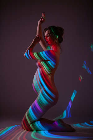 Pregnant woman poses gracefully with colorful light patterns on her bodyの写真素材