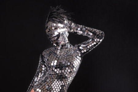 Dancer in a sparkling mirror costume poses dramatically against a dark backdropの写真素材