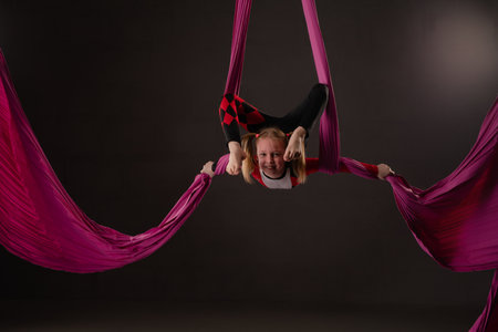 Girl performs aerial acrobatics using pink fabric at indoor studioの写真素材
