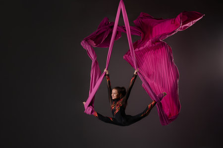 Young girl performs aerial silks routine with vibrant pink fabricの写真素材